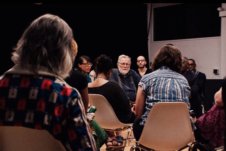 People sit around in white chairs in a still from the film The Task.